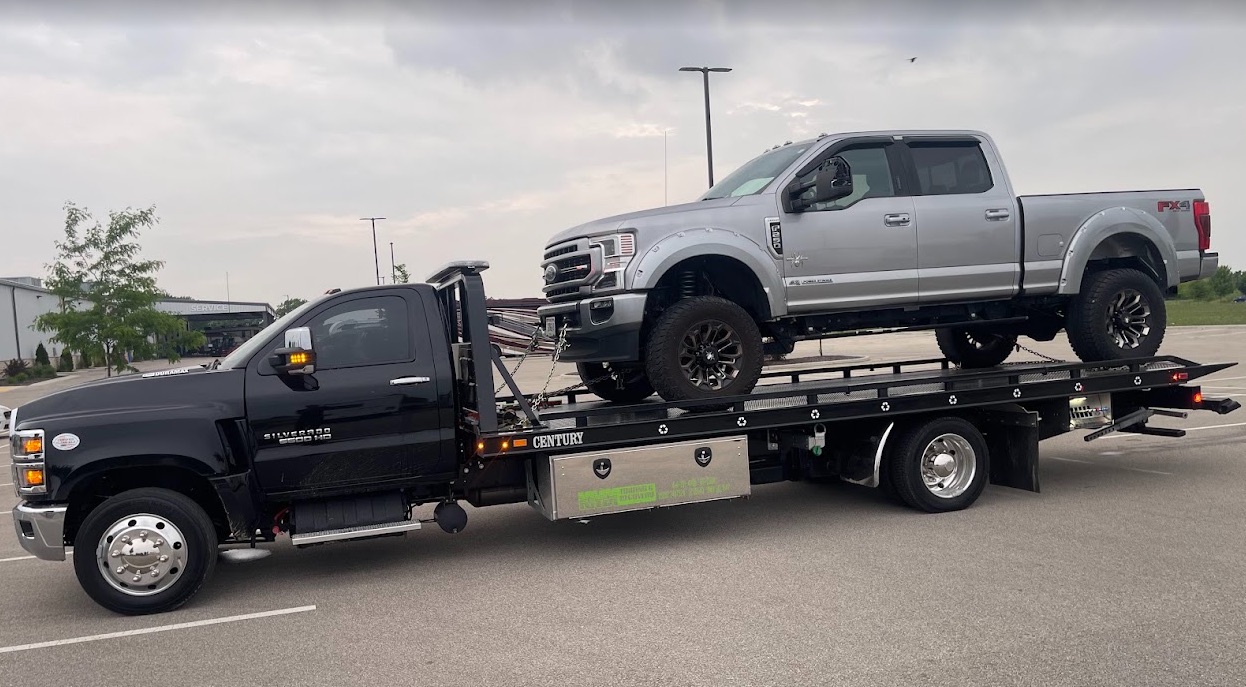 KMK black Century flatbed carrying a silver Ford pickup