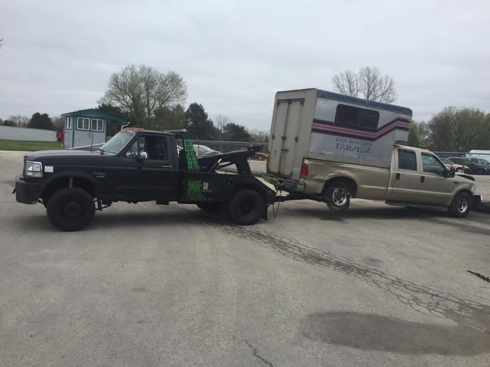 KMK black wrecker with green decals towing a gold Ford pickup